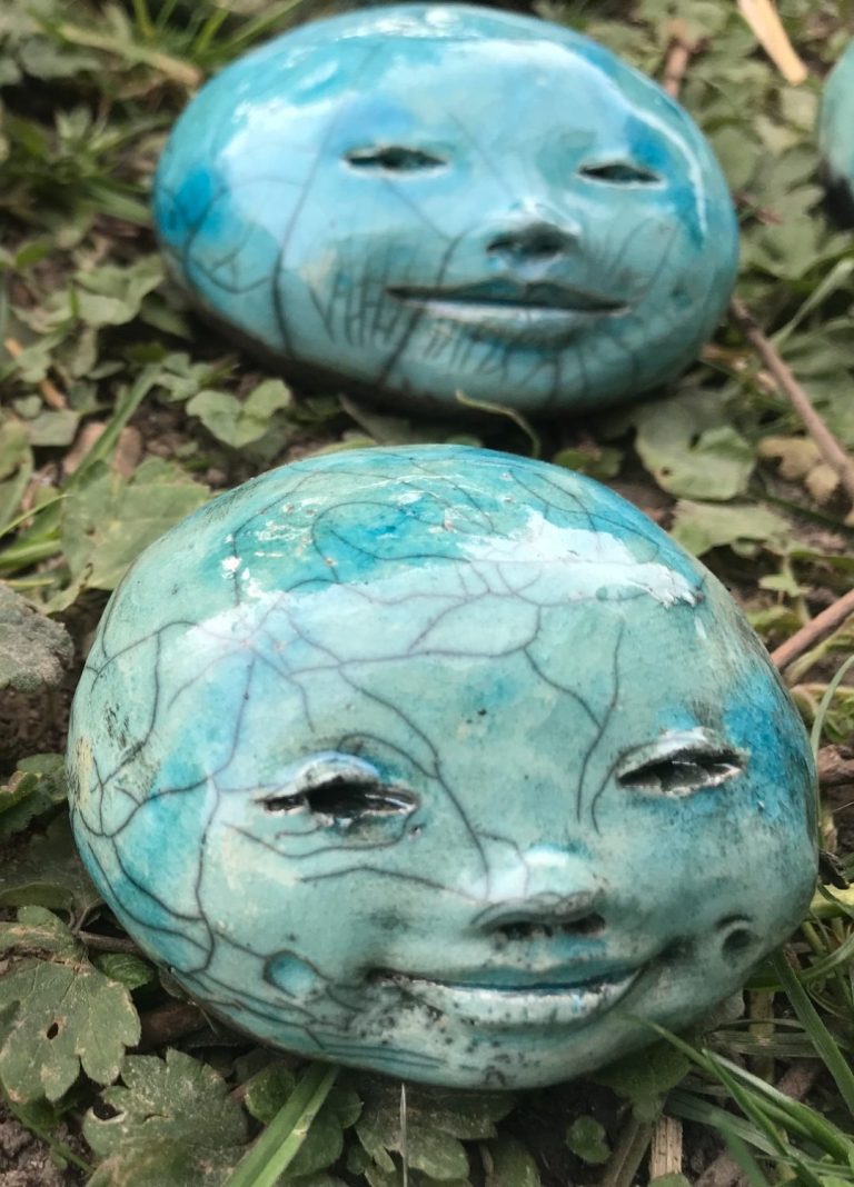 Création "Bonne Bouille" avec des visages sculptés, posés sur un sol herbeux.